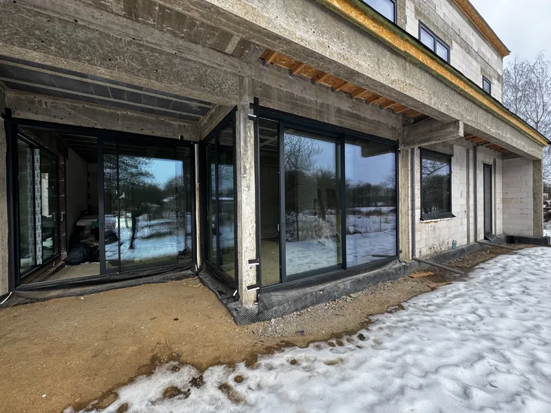 Aluminiowe okna i drzwi rozsuwane HST w czarnej ramie zamontowane w ścianach z gazobetonu i wieńcu żelbetowym, zima, śnieg na zewnątrz — stan surowy zamknięty