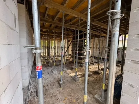 Szalunki stropu żelbetowego od dołu — stalowe podpory teleskopowe podtrzymujące płyty szalunkowe pod stropem monolitycznym, widok techniczny z wnętrza parteru w stanie surowym